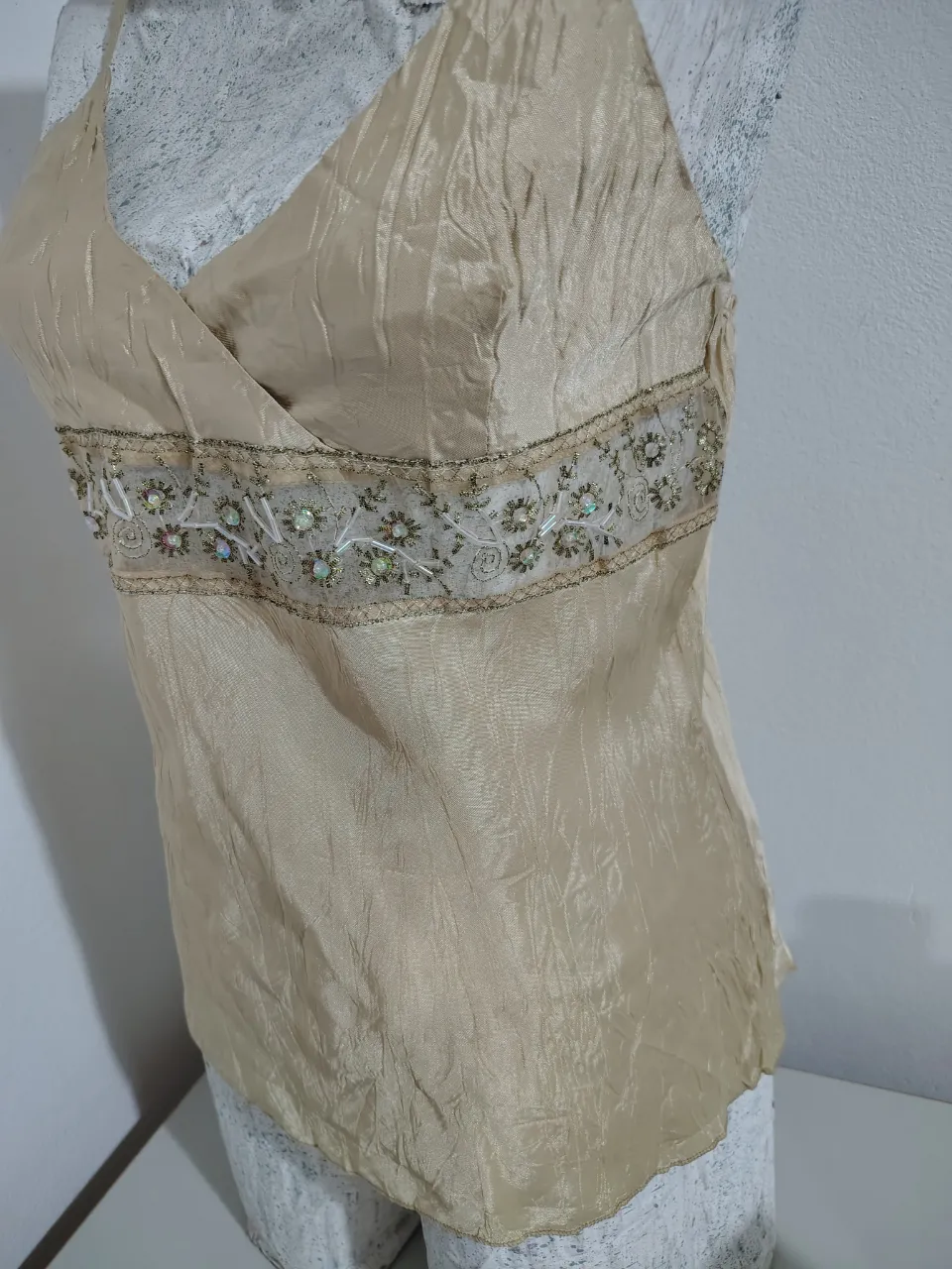 Top de seda color champagne con detalles bordados y pedrería en la cintura. Diseño cruzado en el busto y tirantes finos. Ideal para un look elegante y sofisticado.