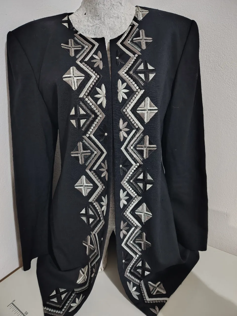 Blazer negro con bordados geométricos en blanco y gris. Diseño abierto al frente, ideal para un look elegante y sofisticado.