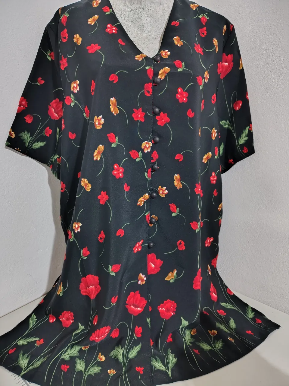 Blusa negra con estampado floral de flores rojas y amarillas. Posee botones al frente y cuello en V. Ideal para un look casual y fresco.