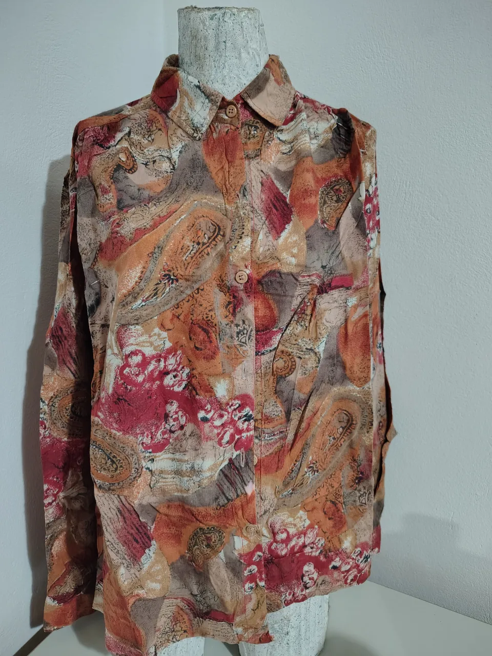 Camisa estampada con un diseño abstracto y floral en tonos tierra, naranja y rojo. Posee cuello clásico y botones al frente. Ideal para un look casual y con un toque vintage.