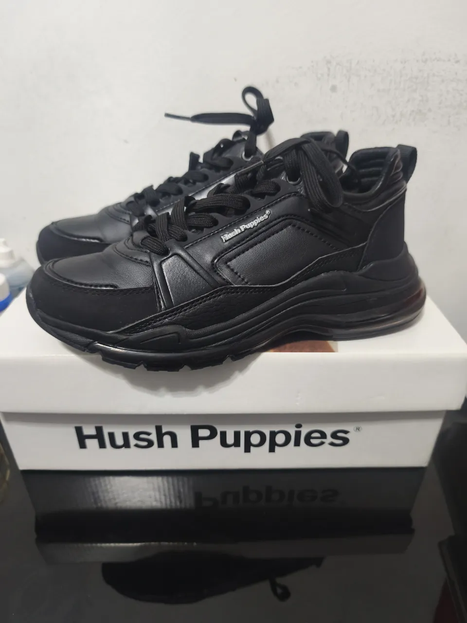 Zapatillas Hush Puppies negras para mujer, con diseño moderno y suela gruesa. Ideales para un look casual y cómodo.