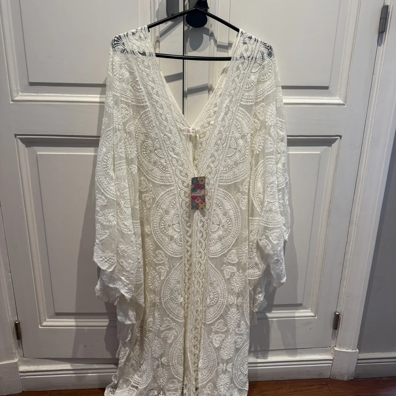 Prenda de encaje blanca, ideal para usar sobre la bikini en la playa o como salida de baño. Su diseño delicado y vaporoso la hace perfecta para un look bohemio y relajado. Se abrocha al frente con un lazo fino. 