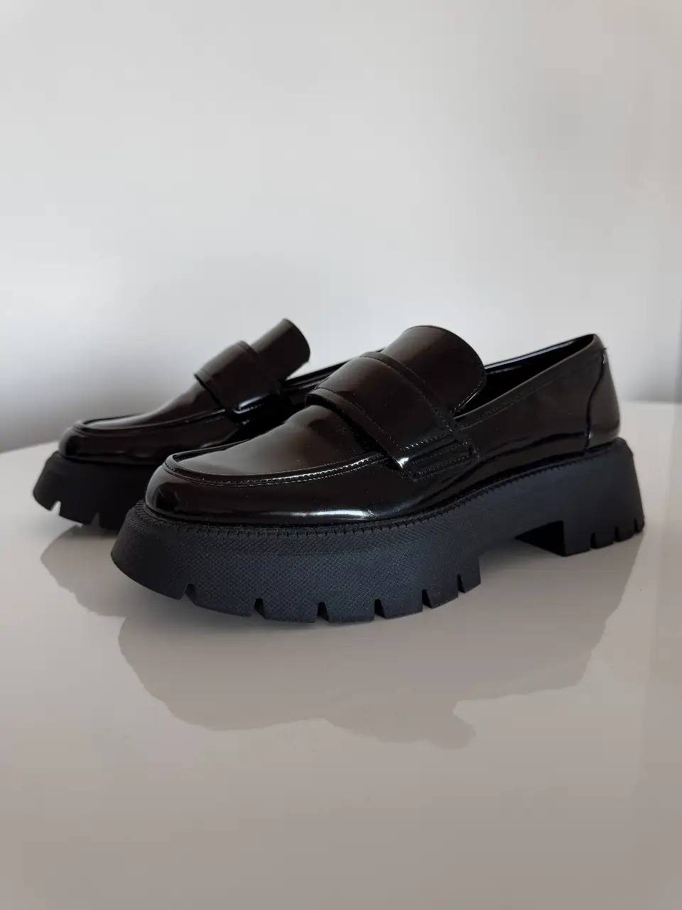 Zapatos tipo mocasín de charol negro con suela track. Tienen un diseño elegante y moderno, ideales para un look sofisticado y a la moda.