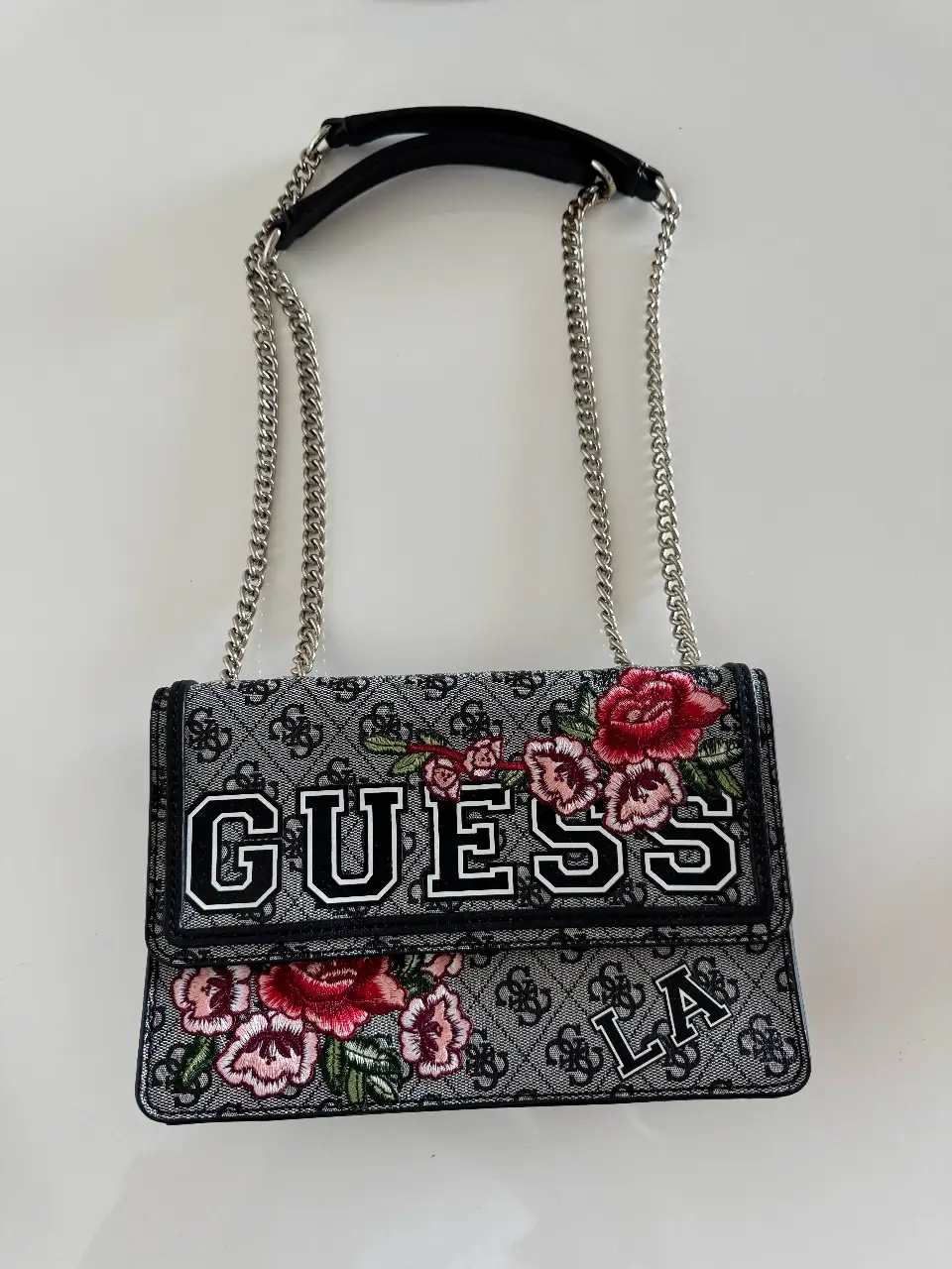 Cartera Guess con estampado del logo de la marca y flores bordadas. Tiene correa de cadena regulable para usarla al hombro o como bandolera y un cierre.