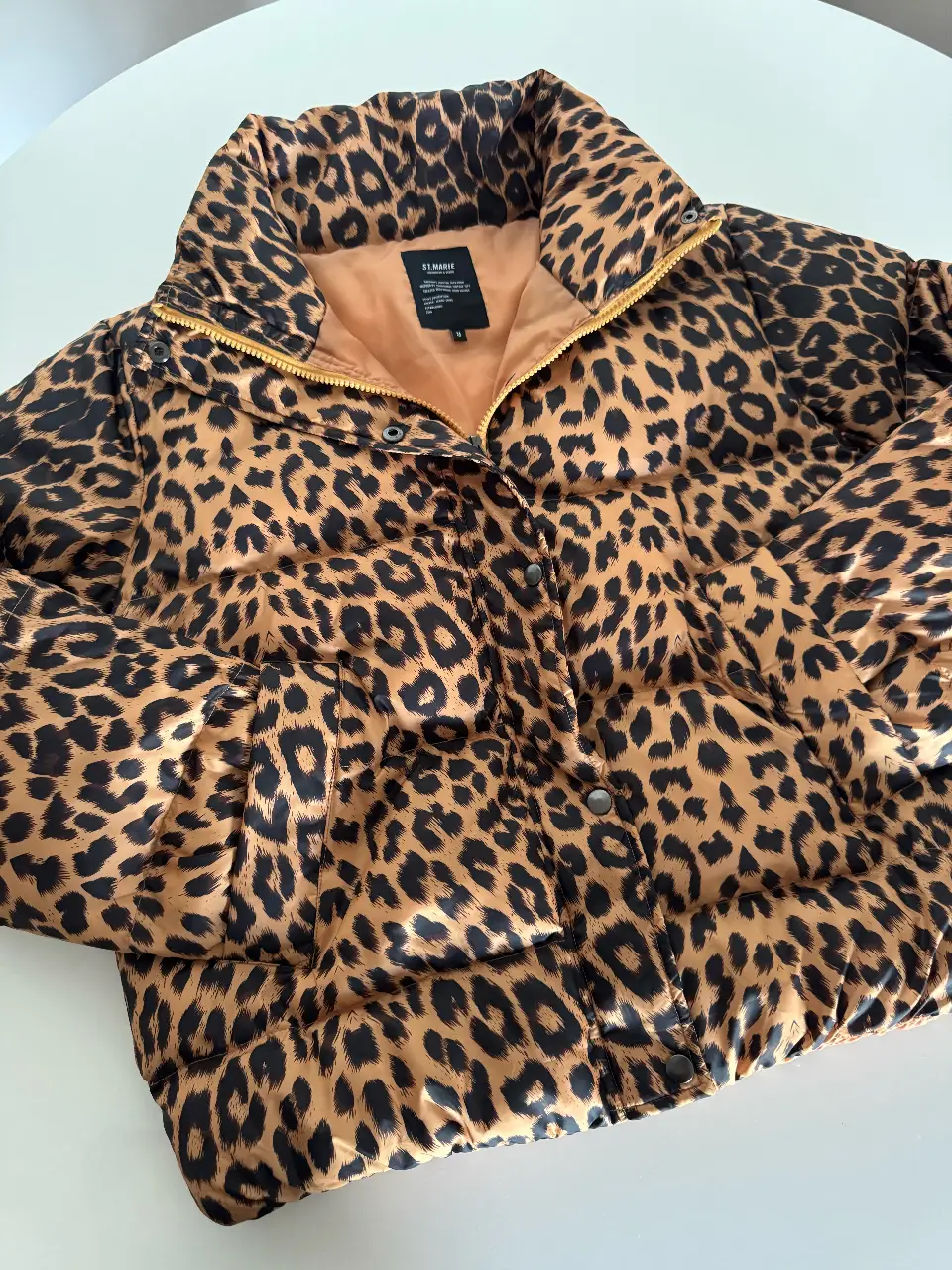 Campera puffer con estampado de animal print, ideal para el invierno. Posee cierre y botones, cuello alto y un forro interior en color durazno. Perfecta para un look canchero y abrigado.