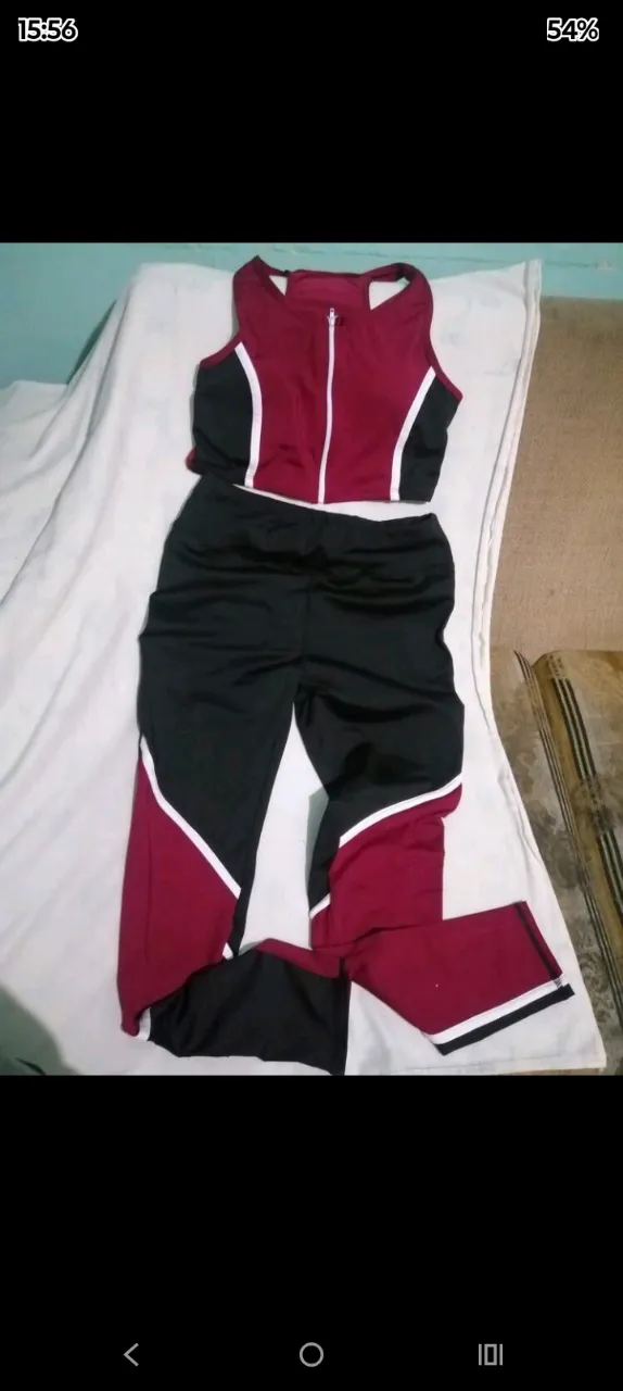 Conjunto deportivo de dos piezas: top deportivo con cierre al frente y pantalón largo. Diseño con recortes en color bordó y blanco sobre fondo negro.