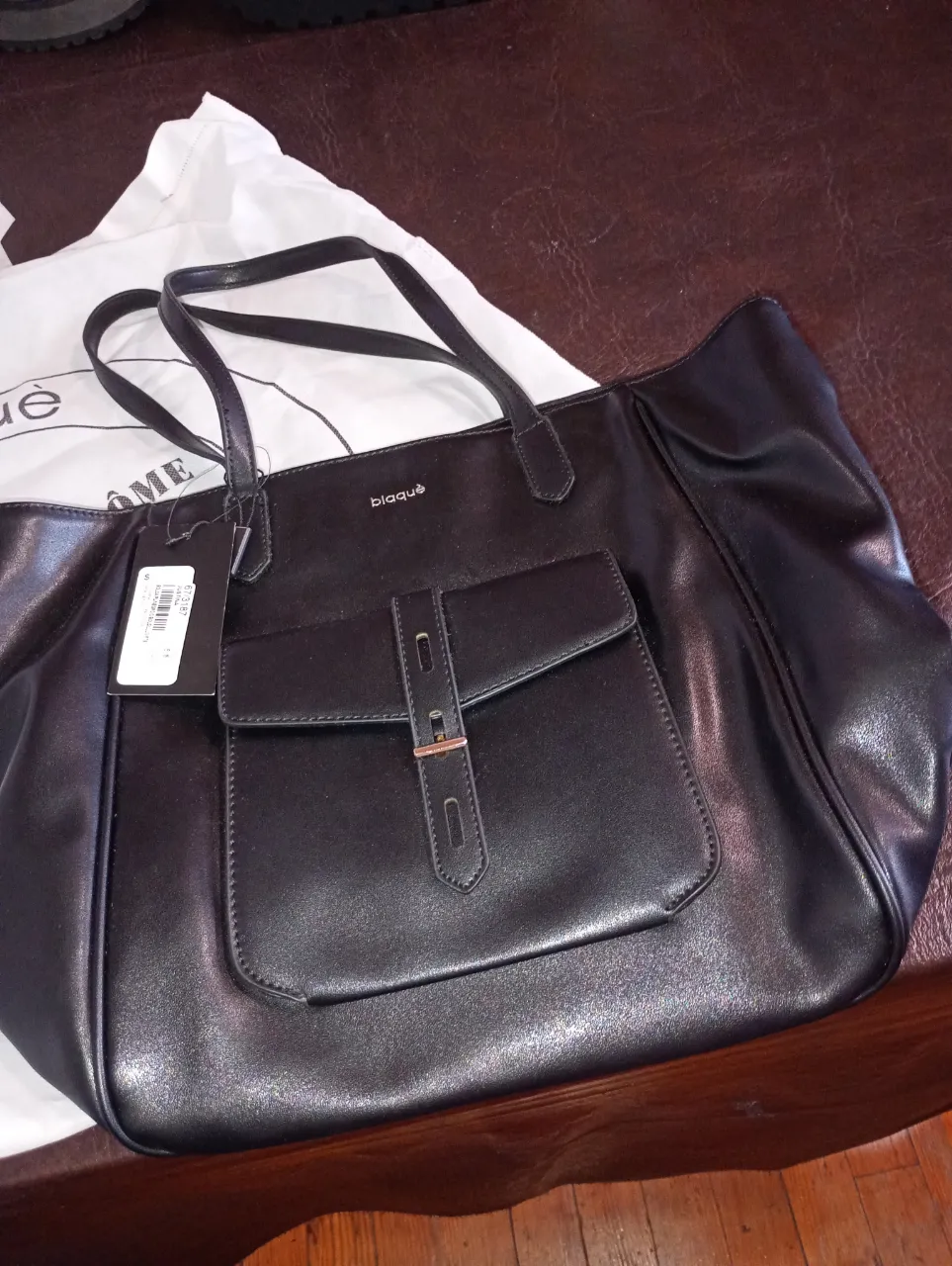 Bolso negro de cuero sintético, con bolsillo frontal y detalles metálicos. Ideal para el día a día o salidas casuales.