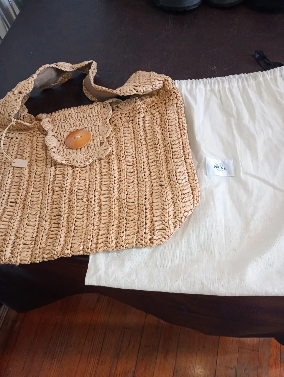 Bolso tejido de paja color natural, con un botón de madera en el frente y manijas reforzadas. Ideal para un look playero o de verano.