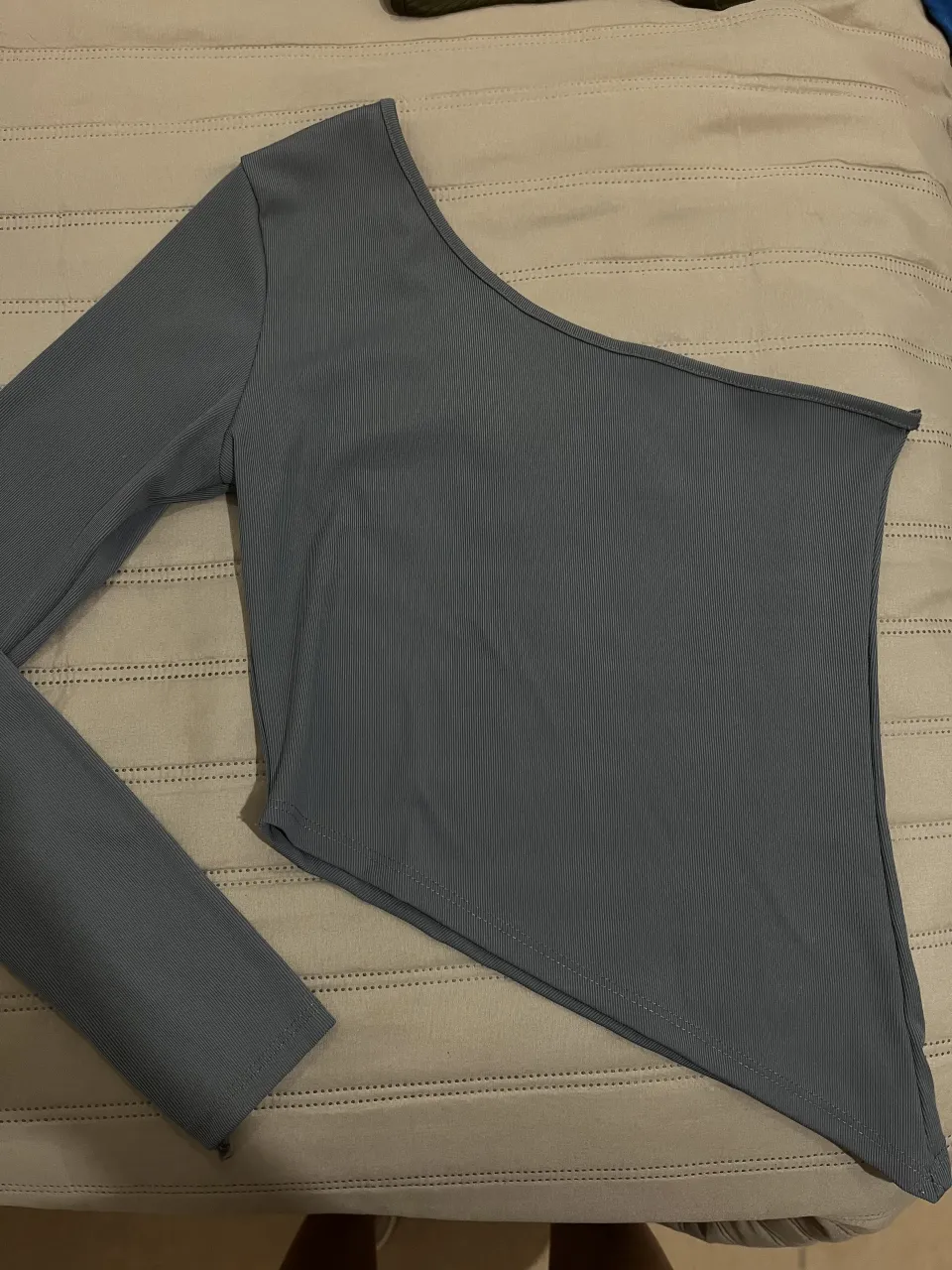 Remera gris asimétrica de manga larga, con un solo hombro descubierto. La tela es (apenas) acanalada.