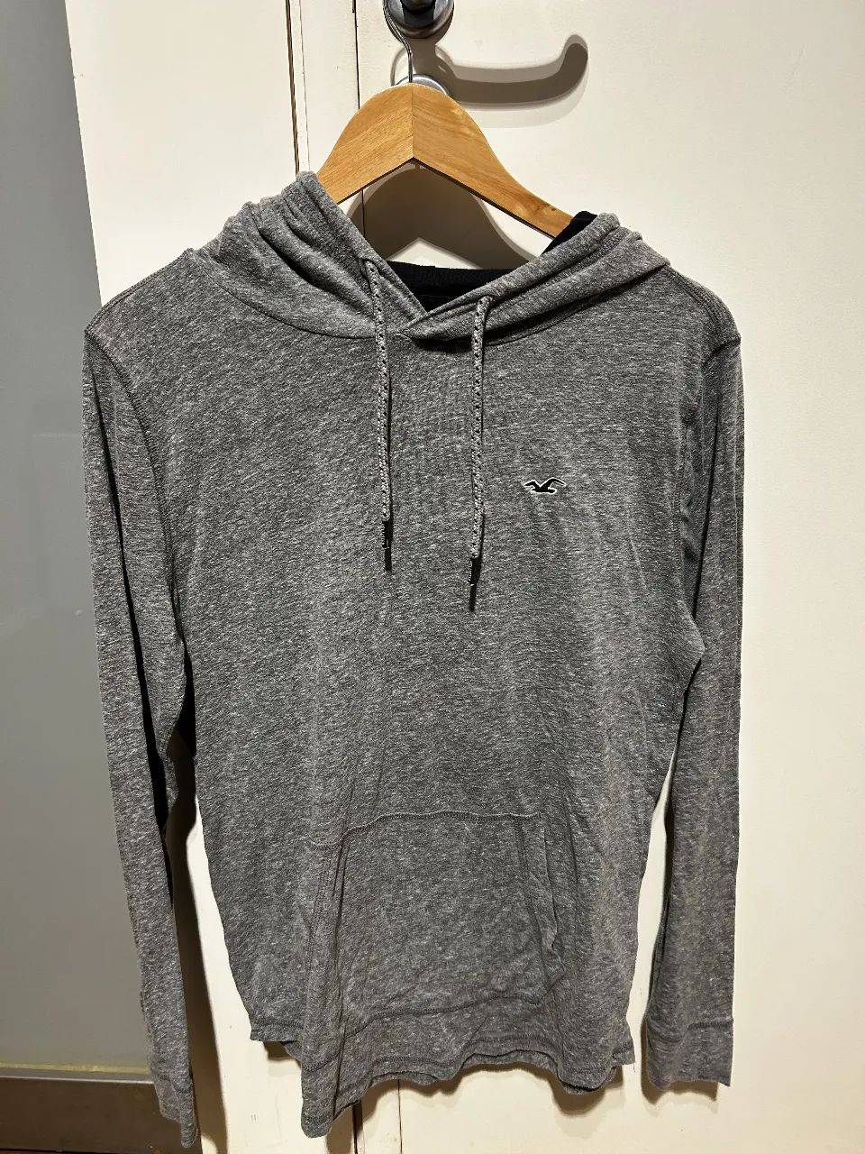 Buzo canguro Hollister gris con capucha y bolsillo delantero. Logo de la marca bordado en el pecho. Interior de la capucha en color negro. Talle S.