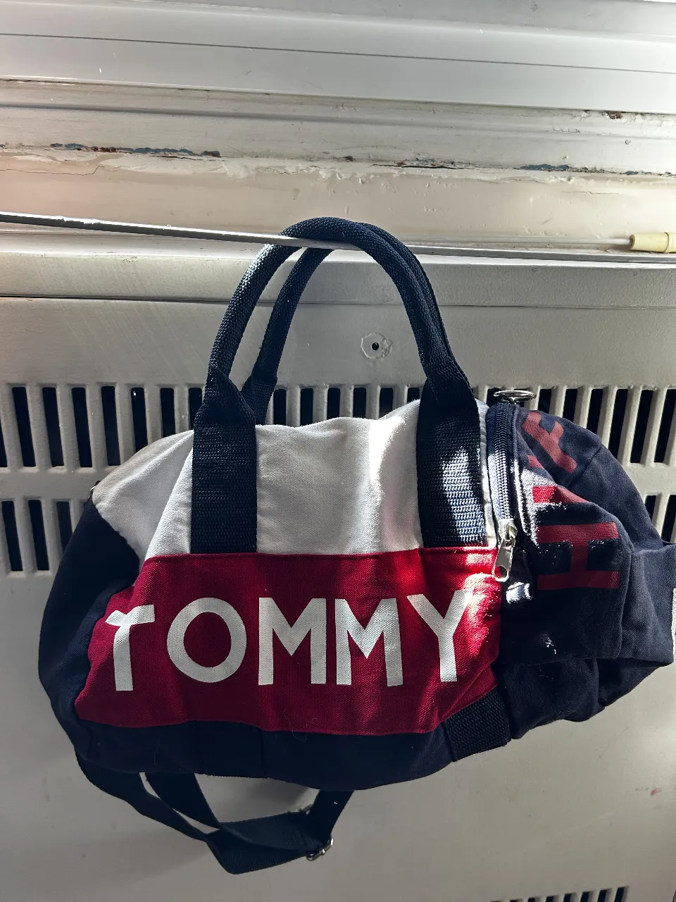 Bolso deportivo Tommy Hilfiger, con diseño icónico en rojo, blanco y azul marino. Cuenta con manijas y correa para el hombro.