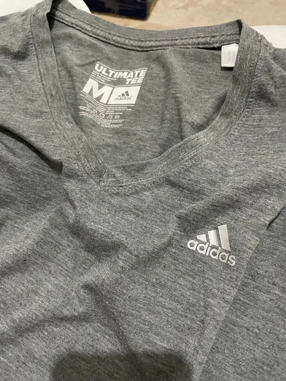 Remera Adidas Ultimate Tee gris para mujer, con cuello en V y logo de la marca en el pecho. Ideal para entrenamientos y actividades deportivas.
