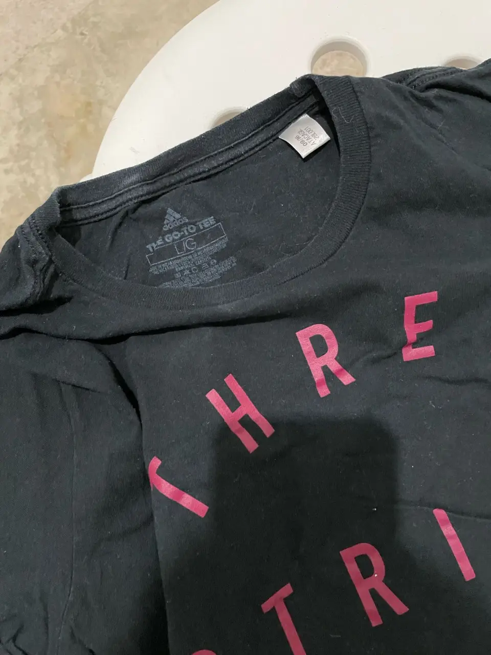 Remera Adidas negra de mujer, con estampado "THREE STRIPE LIFE" en color rosa. Ideal para un look deportivo y casual.