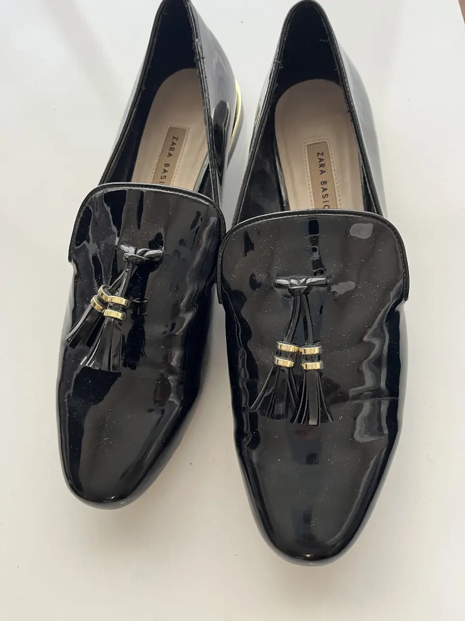Mocasines negros de charol con borlas doradas. Tienen detalles dorados en la parte trasera. Marca Zara Basic.