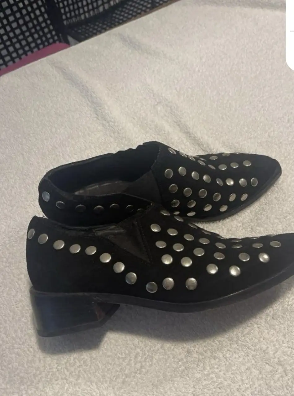 Botines negros de gamuza con tachas plateadas. Tienen un diseño elegante y moderno, ideales para darle un toque rockero a cualquier look. Son cómodos y versátiles, perfectos para usar en diversas ocasiones.