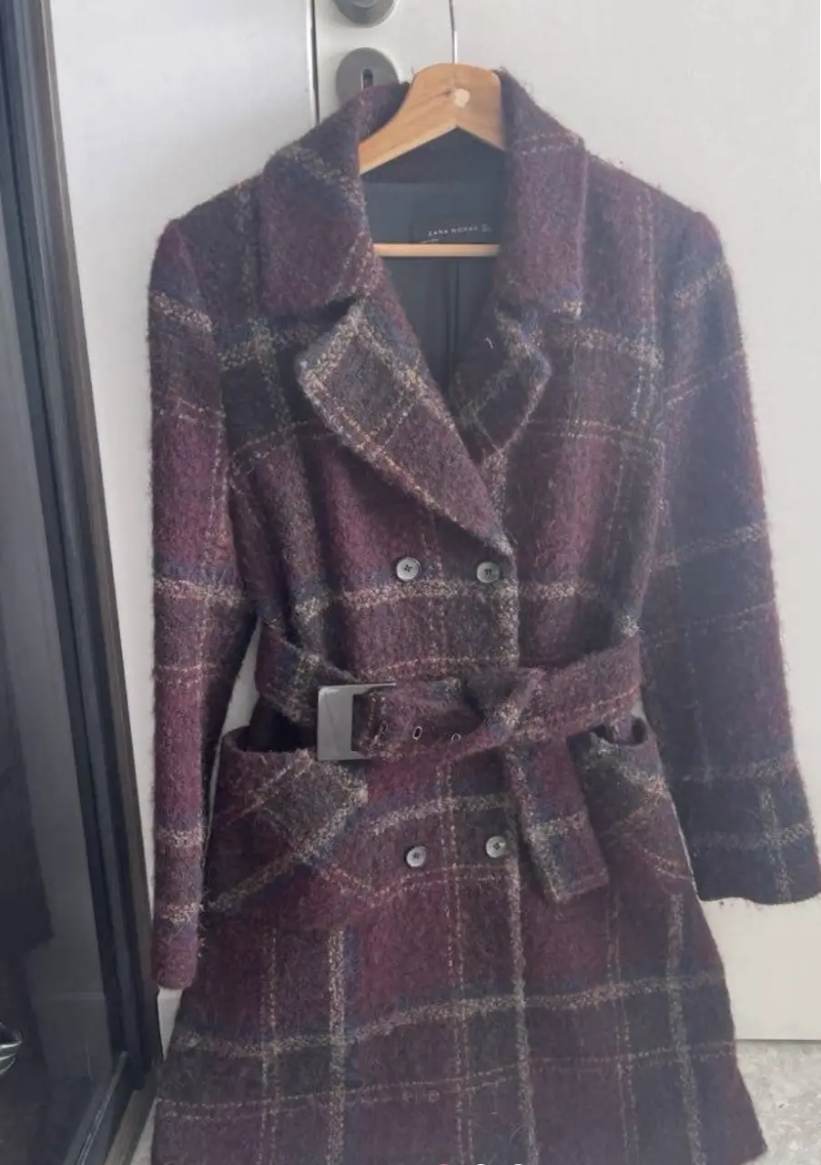 Tapado largo de paño con diseño a cuadros en tonos borgoña y detalles en azul y beige. Posee cinturón para ajustar a la cintura, bolsillos y botones. Ideal para un look elegante y abrigado.