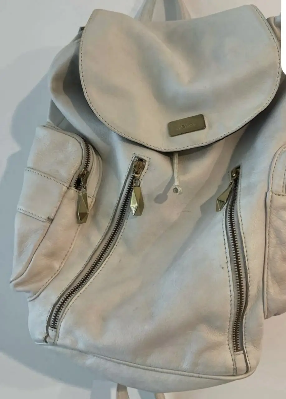 Mochila de cuero blanca con detalles dorados. Cuenta con múltiples bolsillos con cierres y un diseño moderno y funcional. Ideal para llevar tus pertenencias con estilo.