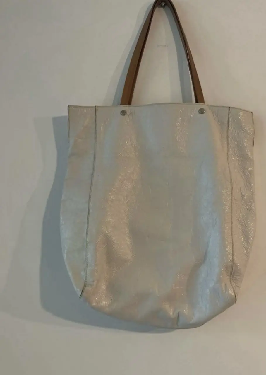 Bolso tote de cuero sintético color crudo, con manijas marrones y detalles metálicos. Ideal para llevar todo lo necesario con estilo.