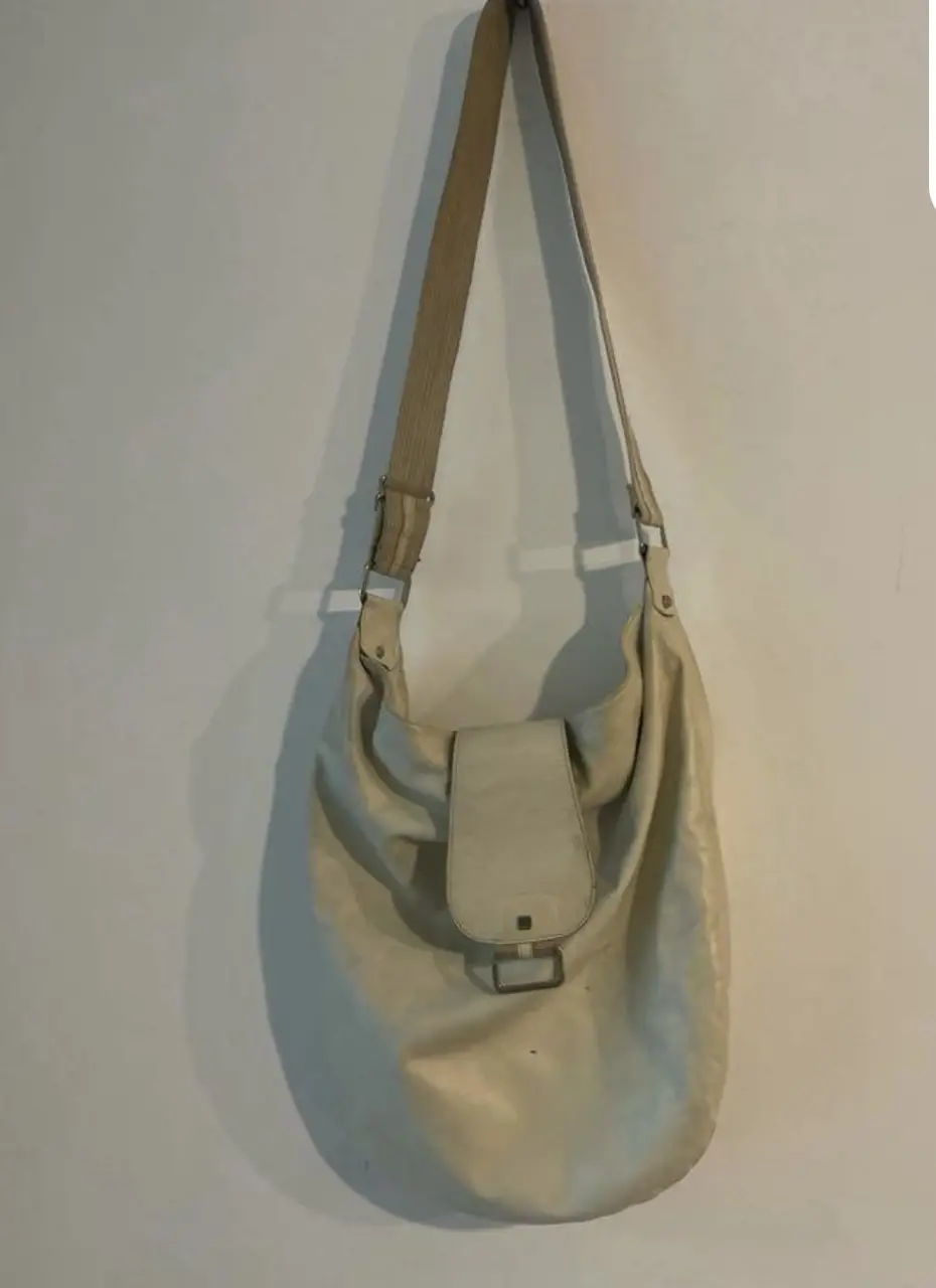 Bandolera de cuero sintético color crudo, con solapa y hebilla metálica. Ideal para un look casual y versátil.