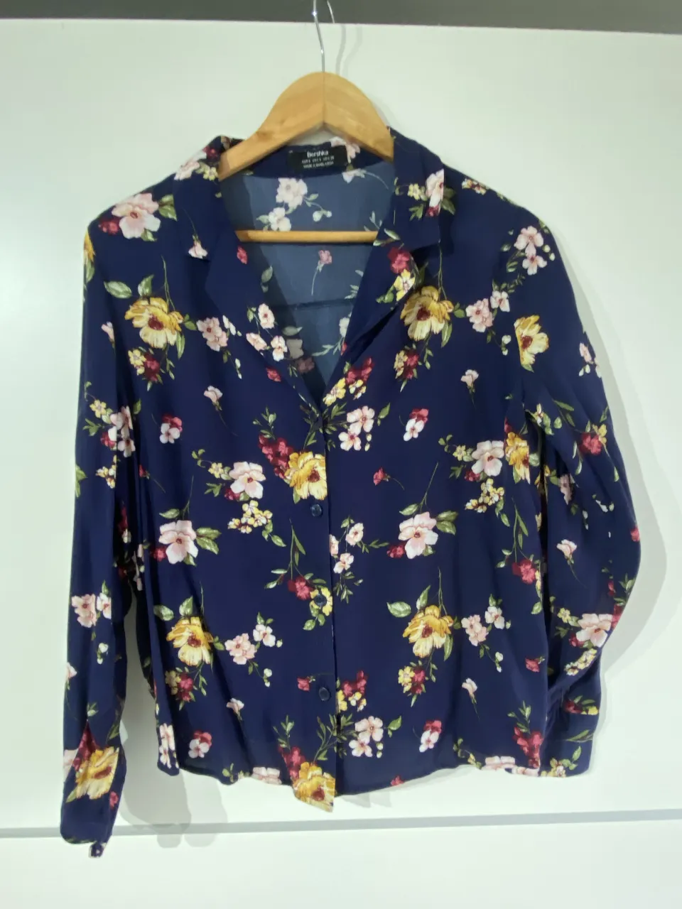Camisa Bershka de mujer, con estampado floral en tonos amarillos, rosas y blancos sobre fondo azul. Manga larga y botones frontales. Ideal para un look casual y femenino.