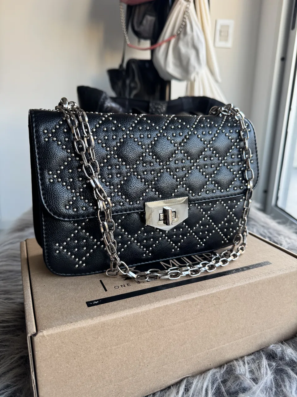 Cartera bandolera negra con tachas plateadas. Diseño acolchado con cadena plateada. Ideal para un look moderno y sofisticado.