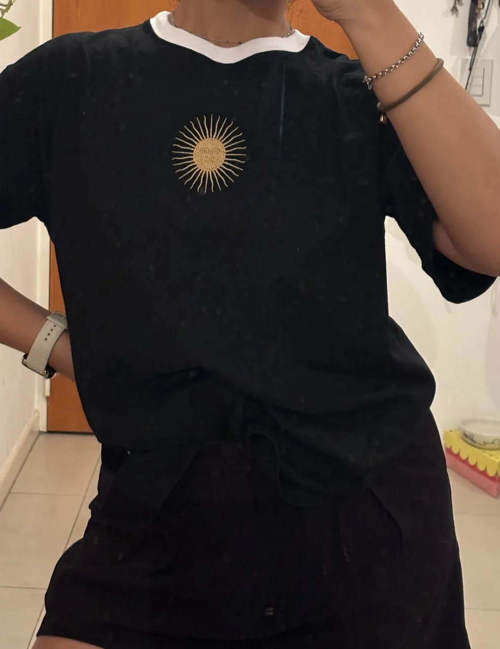 Remera negra con estampa de sol de mayo en el frente. Cuello redondo con detalle blanco. Ideal para un look casual y moderno.