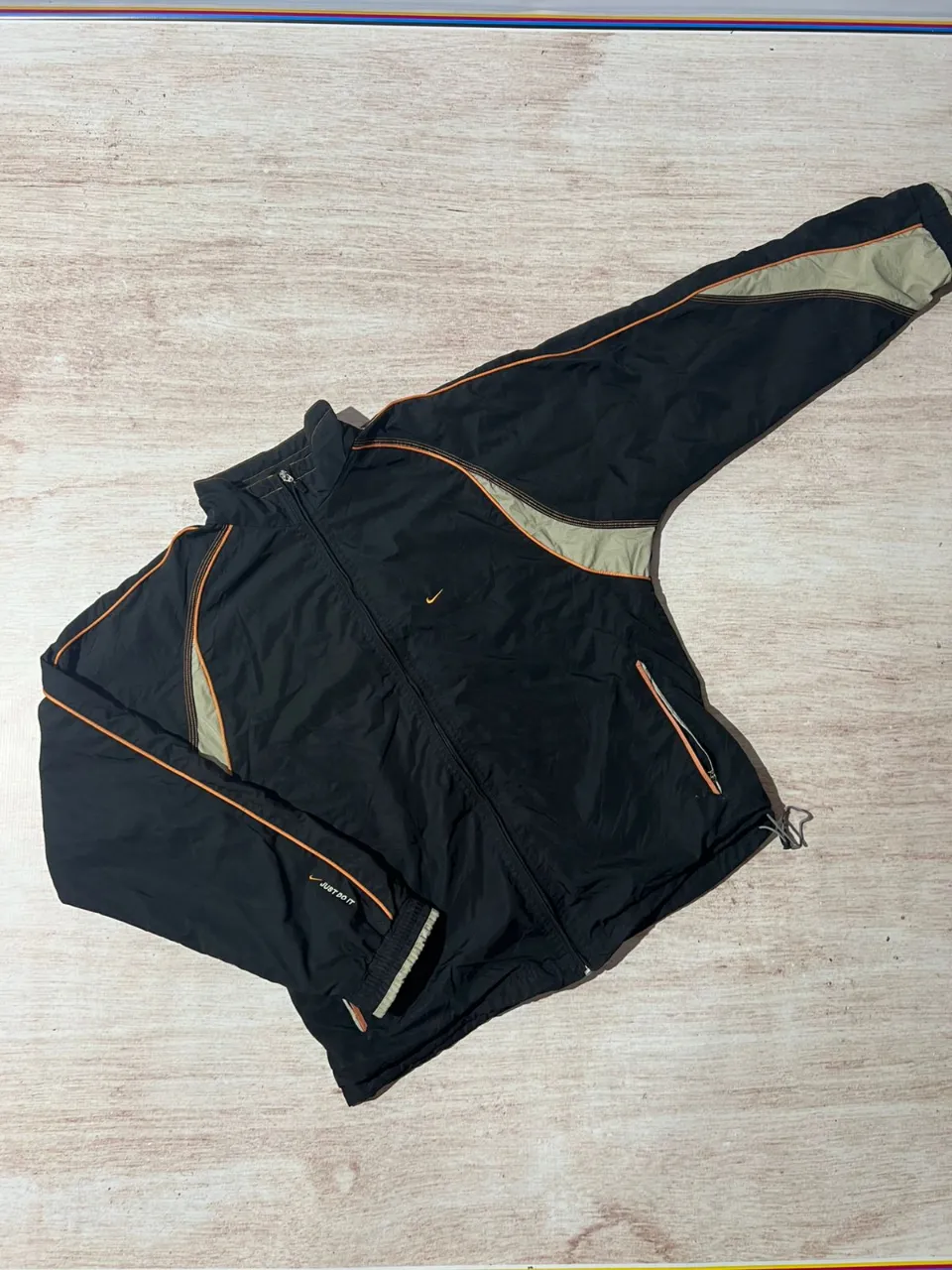 Campera deportiva Nike negra con detalles en gris y naranja. Ideal para entrenamientos o uso casual. Posee cierre completo y bolsillos laterales.