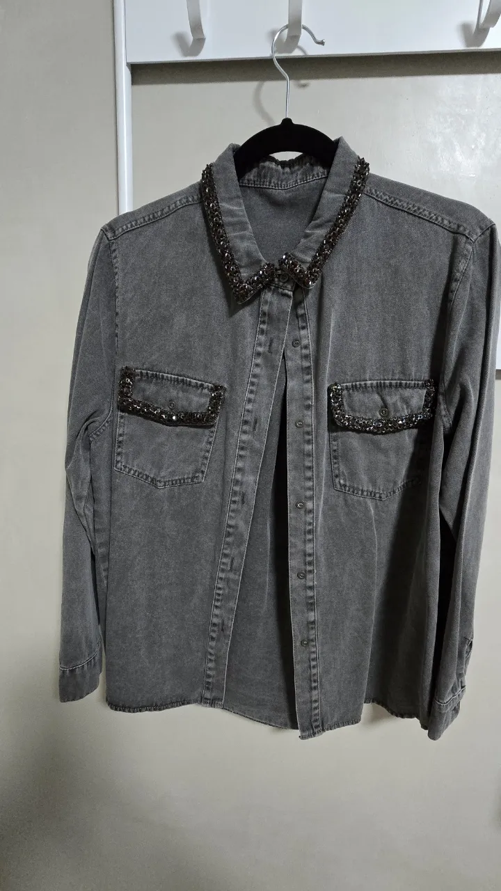 Camisa de jean gris con detalles de pedrería en cuello y bolsillos. Un toque de brillo y glamour para un look canchero y moderno. Ideal para darle un toque especial a tu outfit.