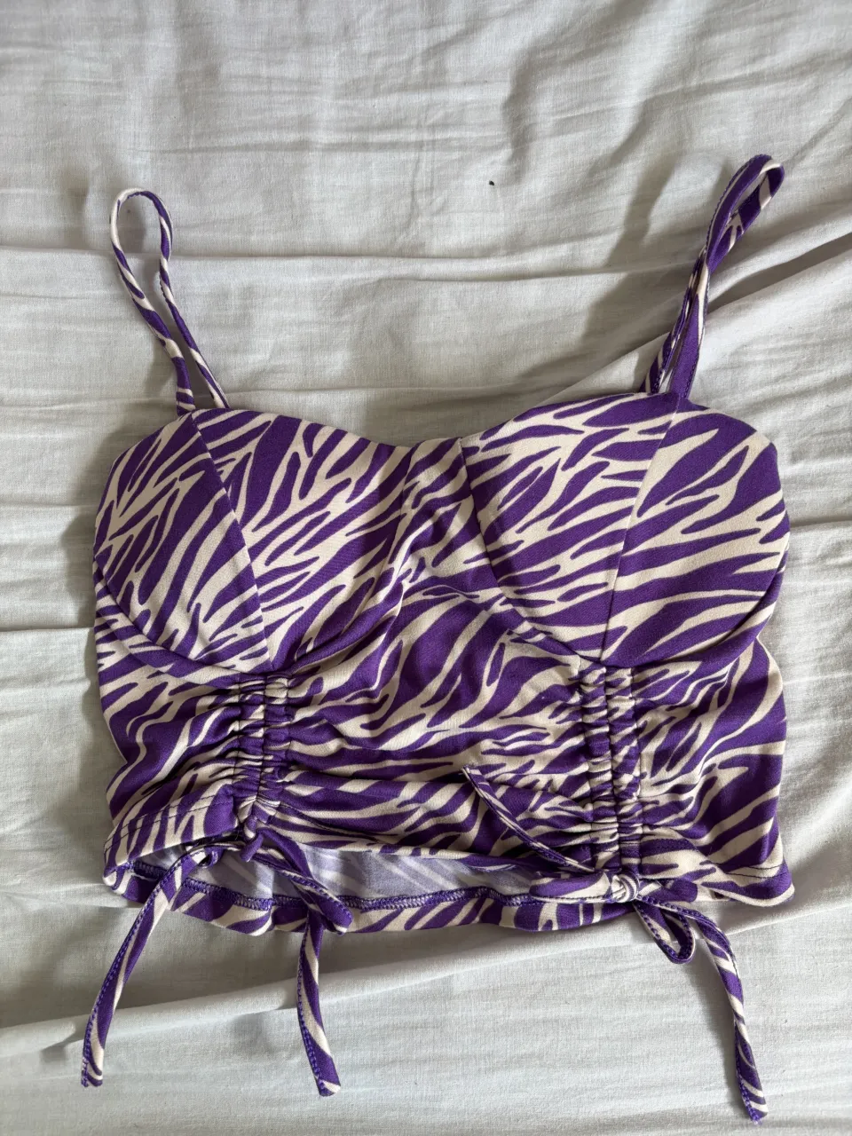 Top súper canchero con estampa de cebra en violeta y blanco. Tiene fruncido y tiras regulables en los laterales para ajustar a tu gusto. Ideal para un look audaz y a la moda.