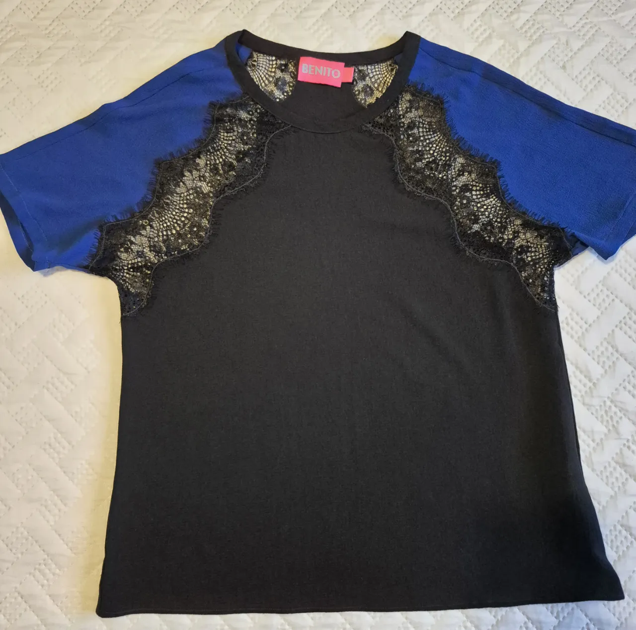 Blusa muy fina, manga corta negra con detalles de encaje en los hombros y mangas de color azul vibrante. Un toque de elegancia y modernidad para tu outfit.