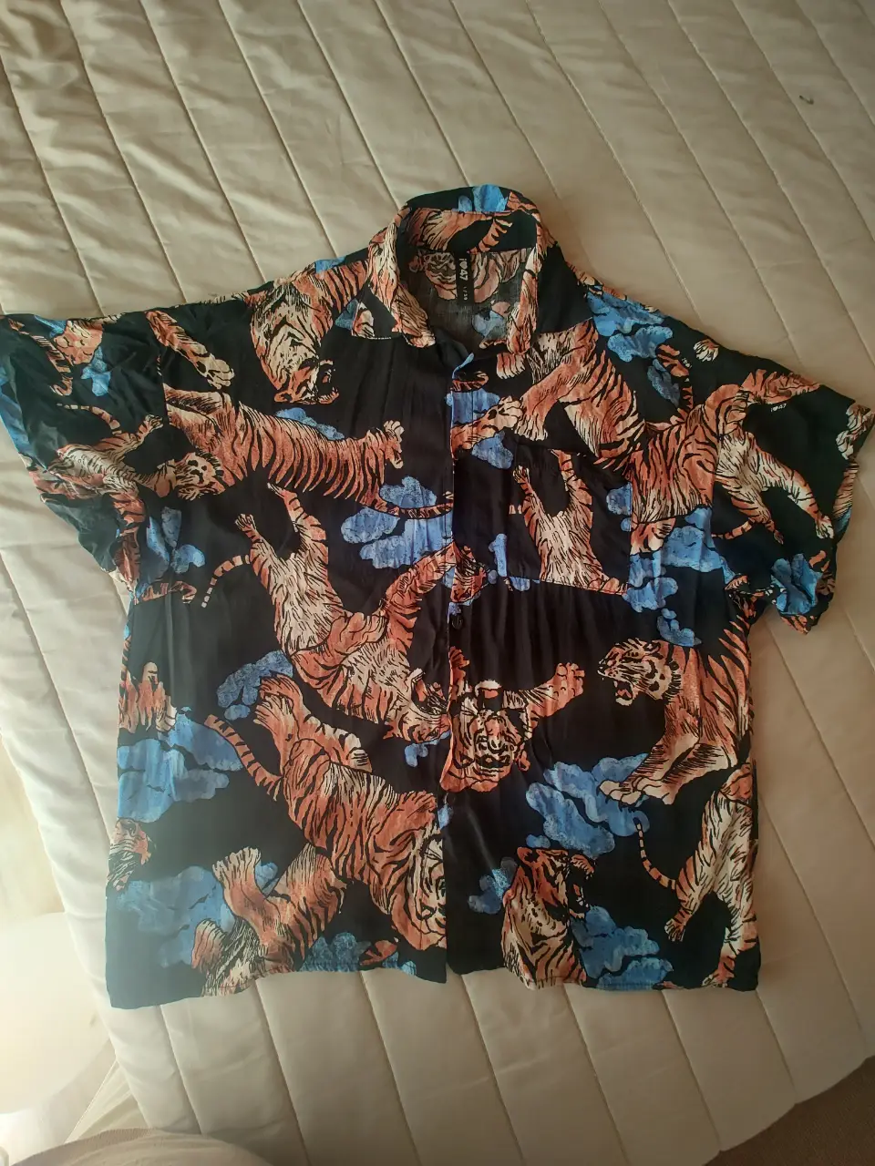 Camisa con estampado de tigres en tonos naranja y azul sobre fondo negro. Ideal para un look casual y con onda. Tiene 62cm de largo y 54cm de ancho