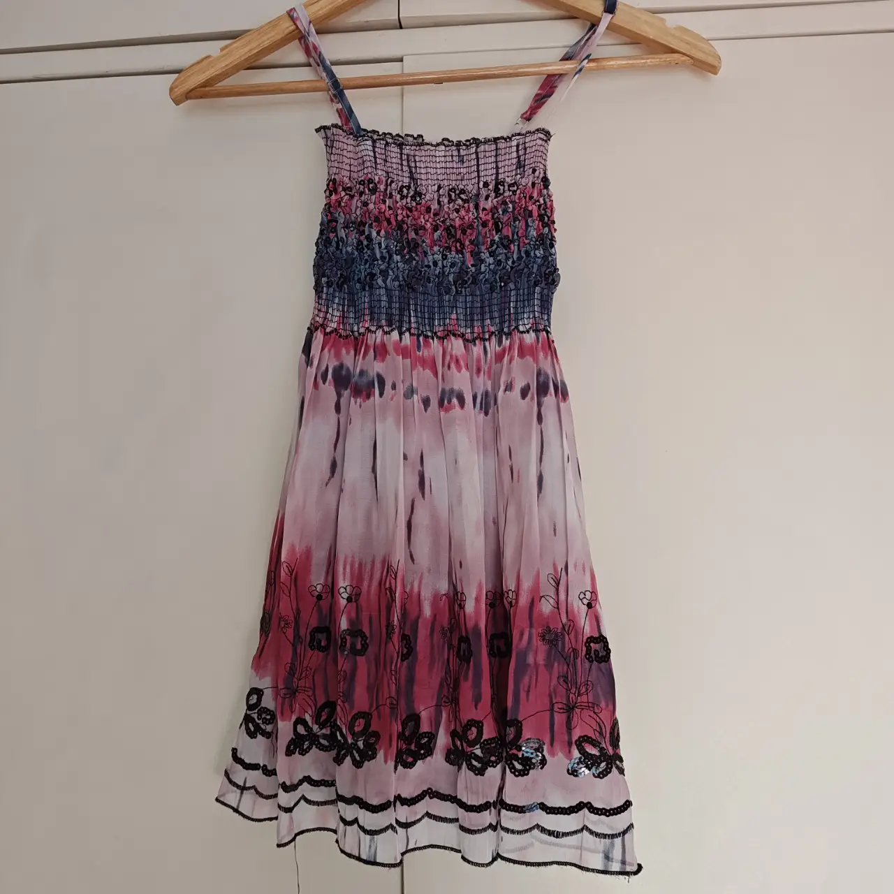 Musculosa, con diseño tie-dye en tonos rosa y negro Tiene el pecho fruncido y tirantes finos. La parte inferior presenta un detalle de flores negras bordadas en lentejuelas.