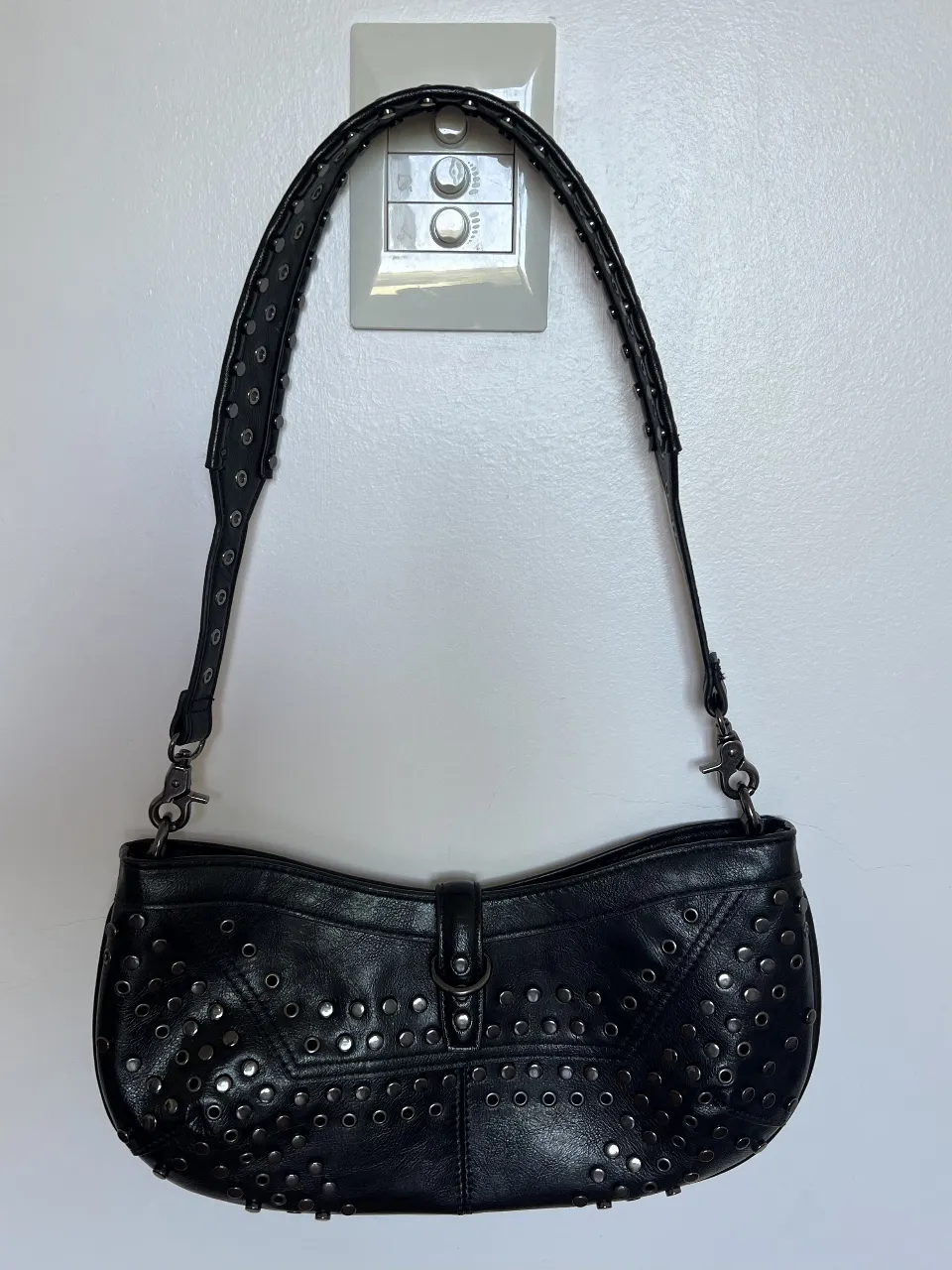 Cartera negra con tachas metálicas plateadas en toda su superficie y en la tira. Cierre con broche.