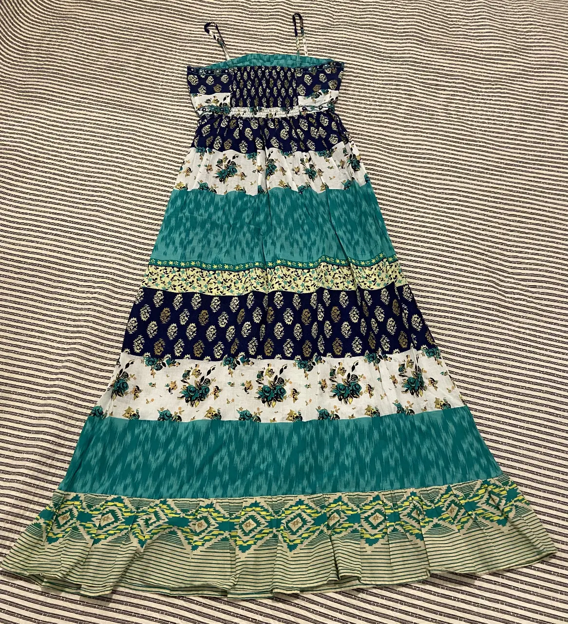 Vestido largo de verano con diseño bohemio. Combina paneles de diferentes estampados florales y geométricos en tonos azules, blancos y verdes. Ideal para un look fresco y relajado.