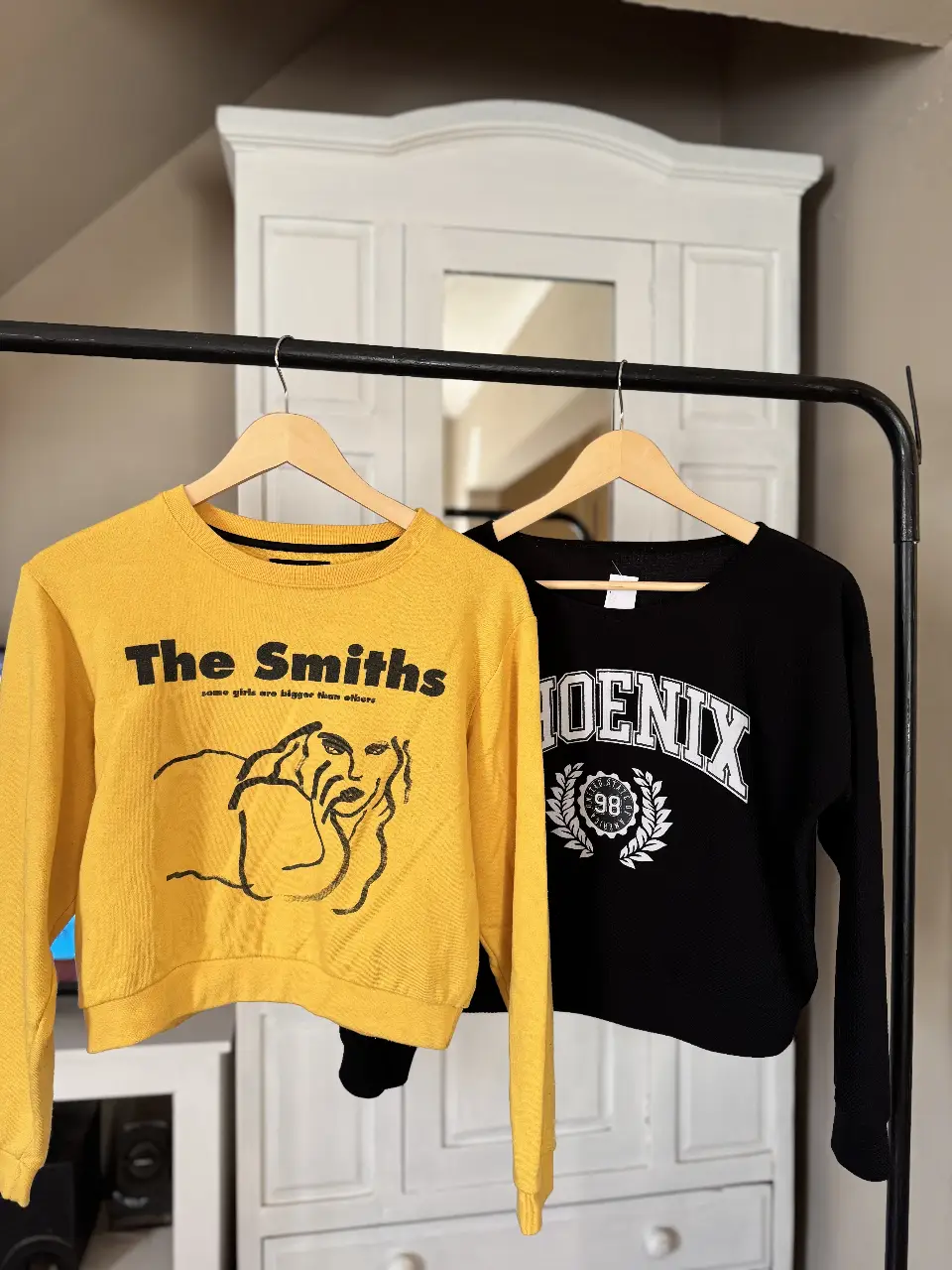 Buzo de cuello redondo amarillo con estampado de "The Smiths" y un diseño artístico. El buzo negro complementario presenta la palabra "Phoenix" y un diseño de laurel. Ideal para un look casual y con estilo.