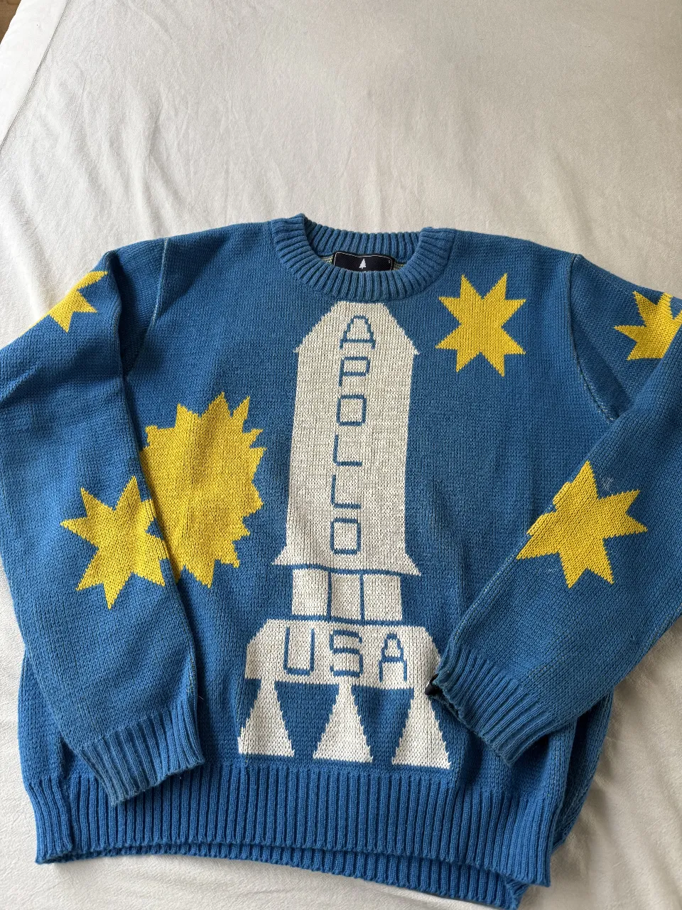 Sweater de lana azul con diseño de cohete y estrellas amarillas. Ideal para un look retro y original. Perfecto para el invierno.