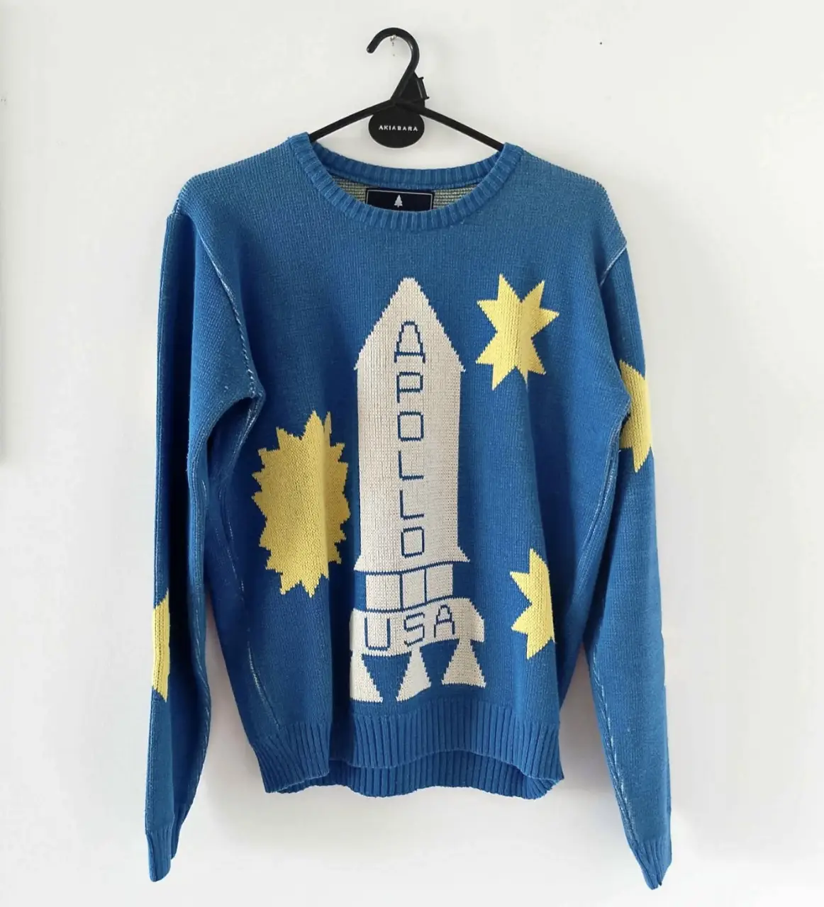 Sweater de lana azul con diseño de cohete y estrellas amarillas. Estilo retro, ideal para un look casual y original. Perfecto para el invierno.