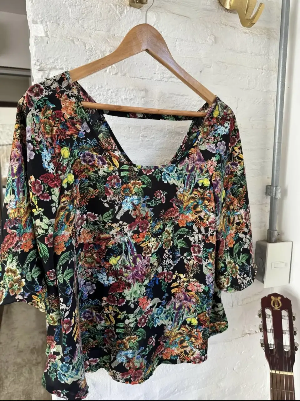 Blusa de mujer con estampado floral vibrante en tonos rojos, amarillos, azules y morados sobre fondo negro. Diseño con escote en la espalda y mangas cortas amplias, ideal para un look bohemio y fresco.