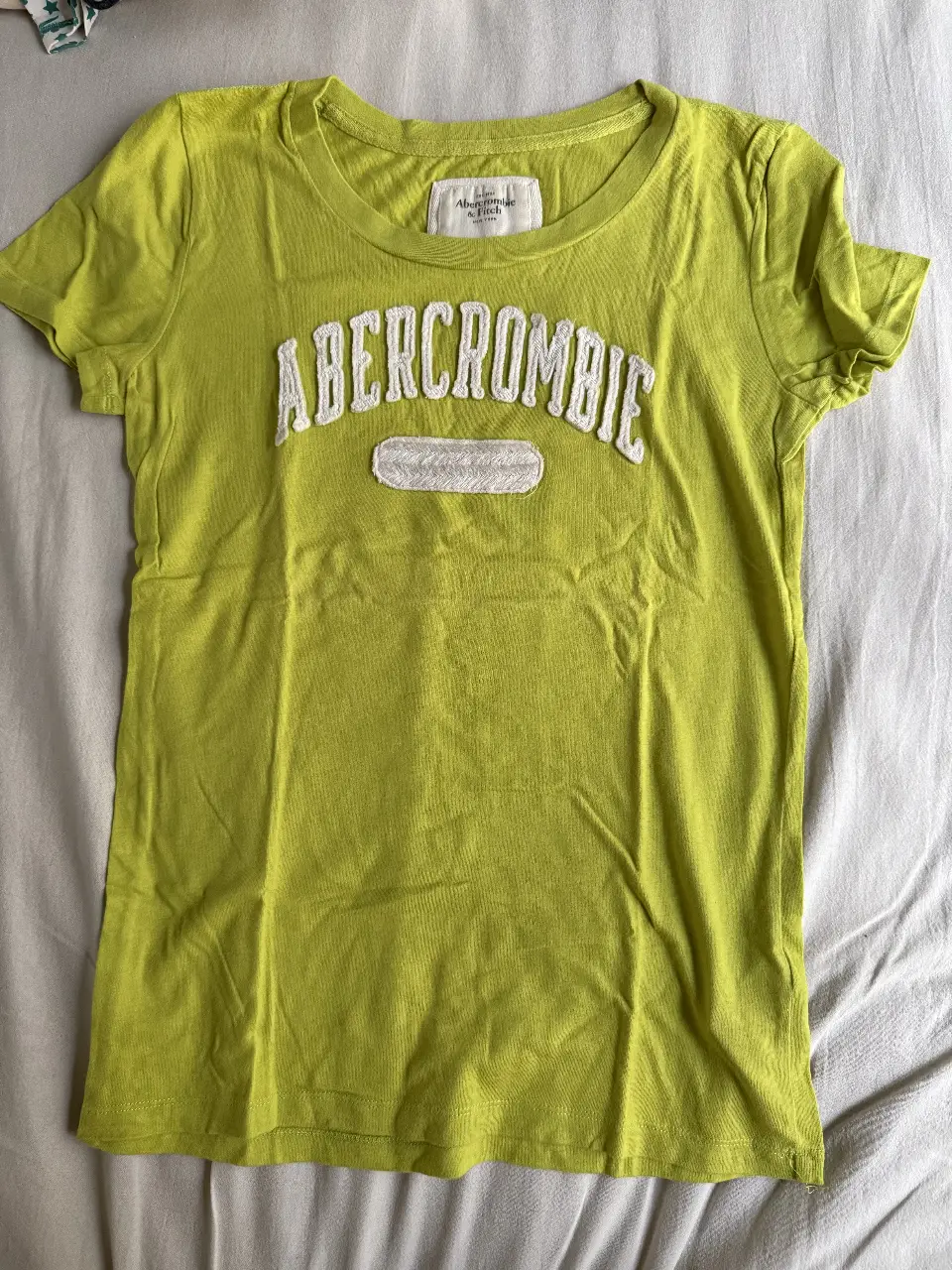 Remera de mujer Abercrombie & Fitch, color verde claro. Con el logo de la marca en relieve en el frente. Ideal para un look casual y cómodo.