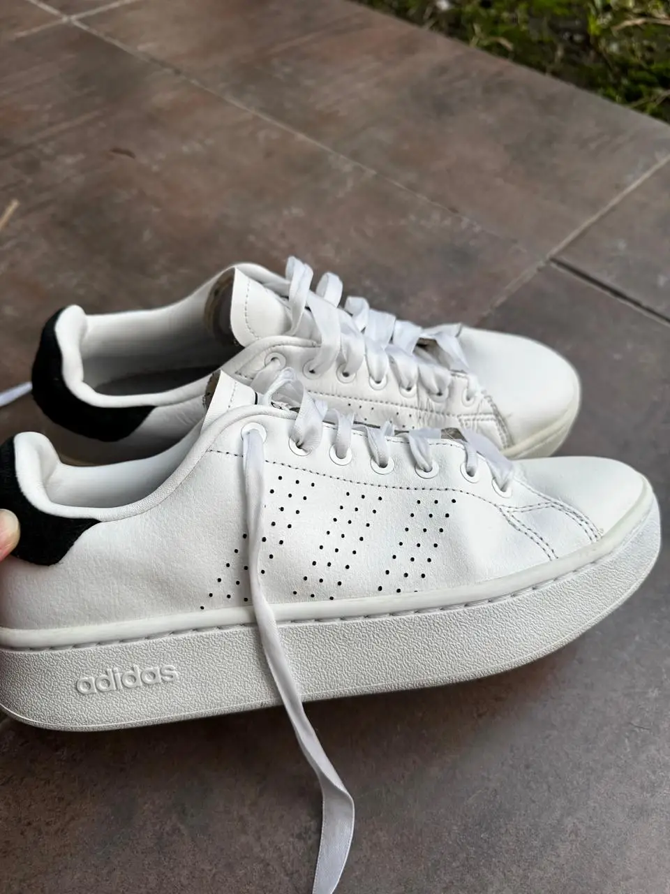 Zapatillas Adidas blancas, modelo Court, con detalles en negro en la parte trasera. Diseño clásico y cómodo, ideales para uso diario.