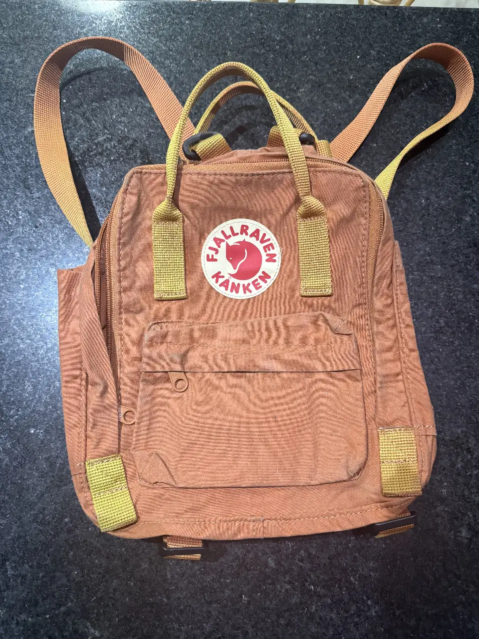 Mochila Fjallraven Kanken clásica en color marrón con detalles en amarillo. Ideal para uso diario, con un diseño icónico y duradero.
