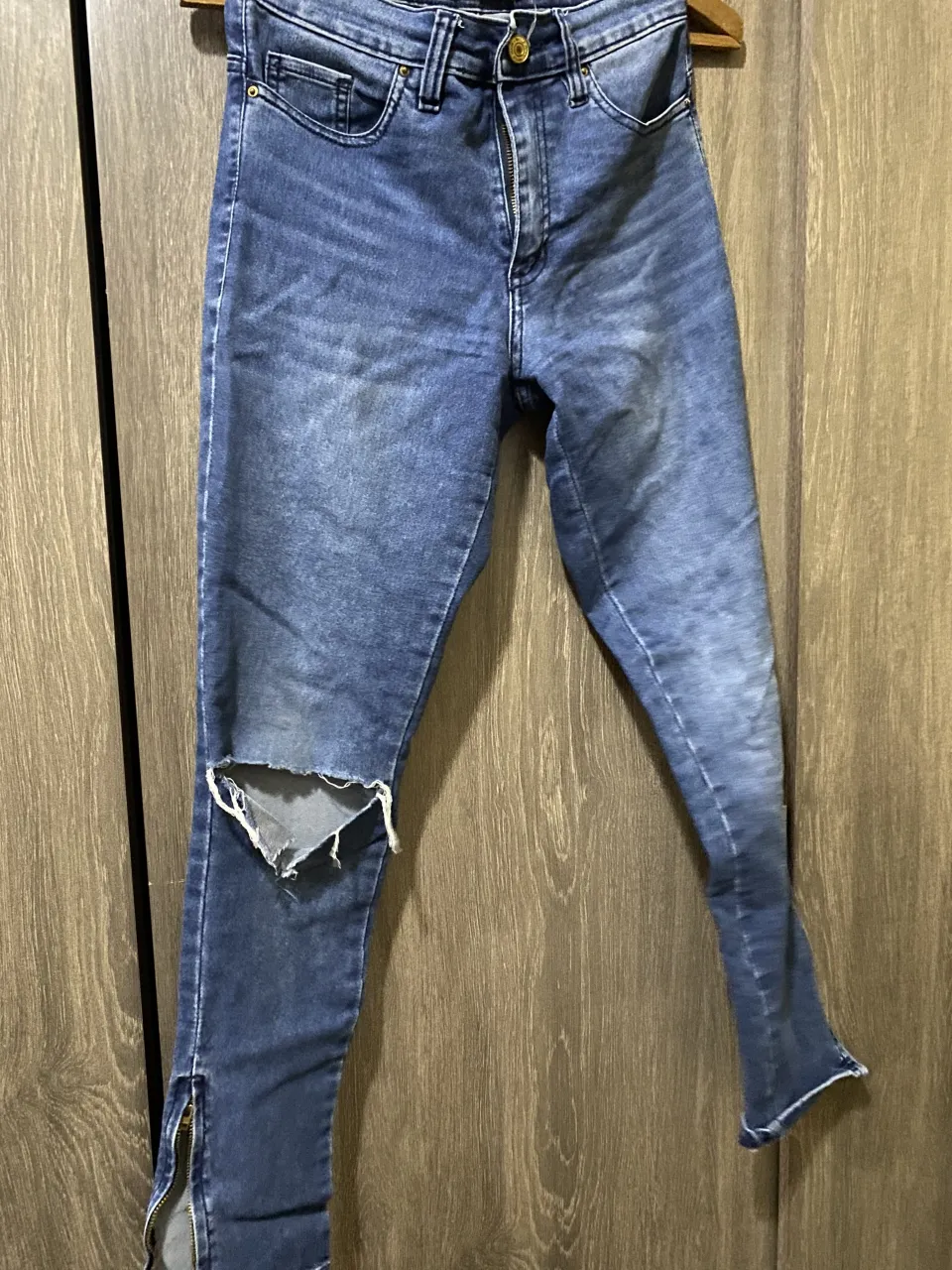 Jeans de tiro alto con rotura en la rodilla izquierda y cierre en los tobillos. Color azul desgastado.