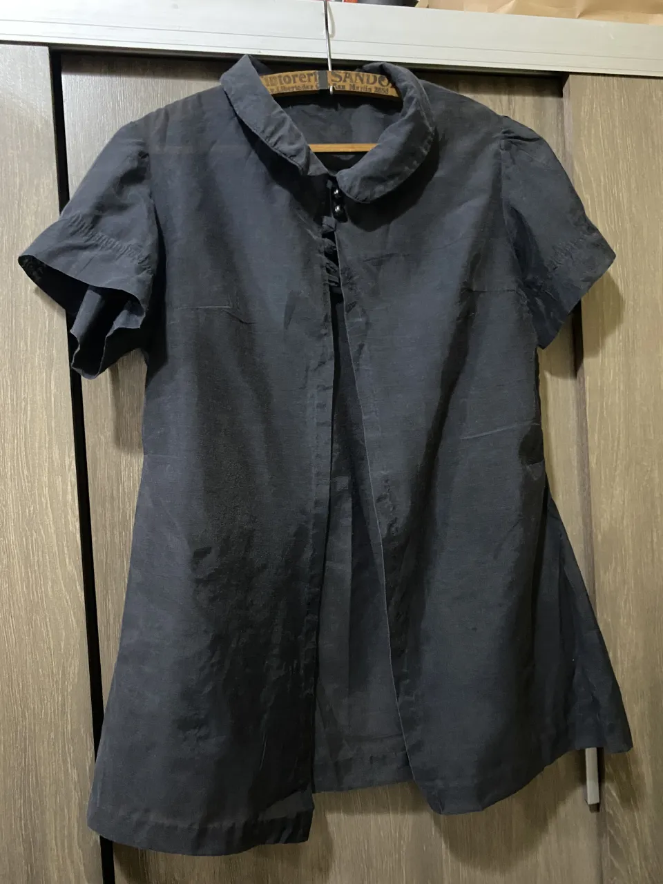 Camisa de color negro con cuello redondo y mangas cortas con volados. Posee botones al frente.