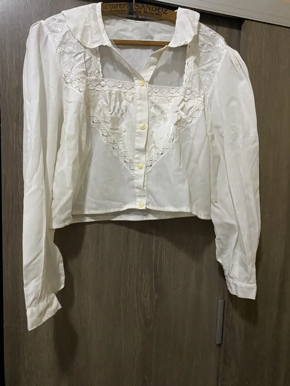 Blusa blanca con mangas largas y detalles de encaje en el frente y cuello. Posee botones al tono en la parte delantera.