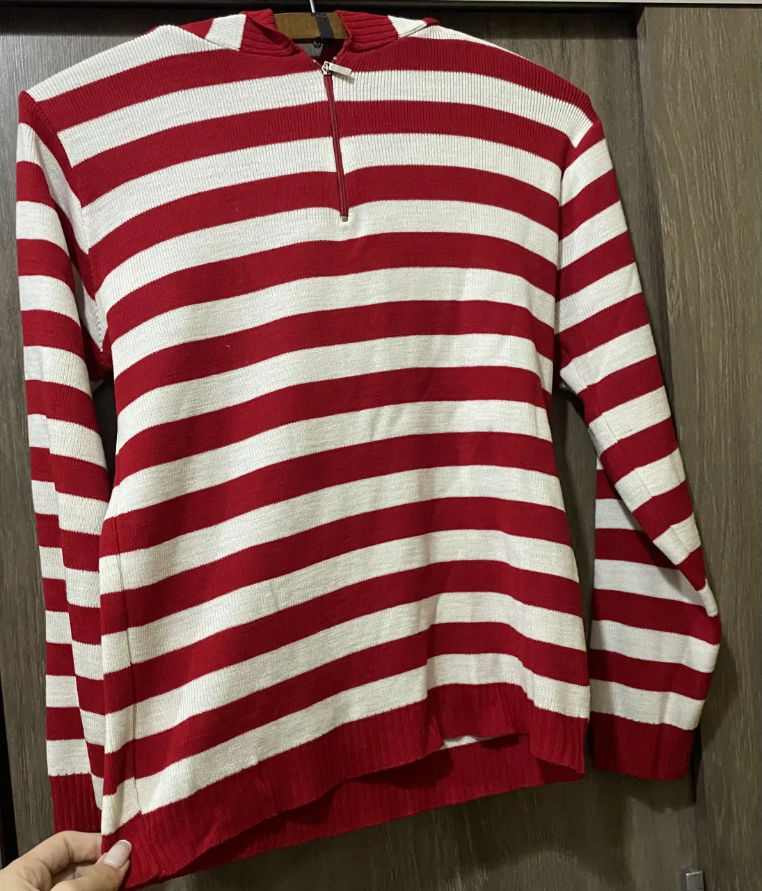 Buzo a rayas rojas y blancas con capucha y cierre en el cuello. Tiene un parche con el logo de la marca en la espalda.