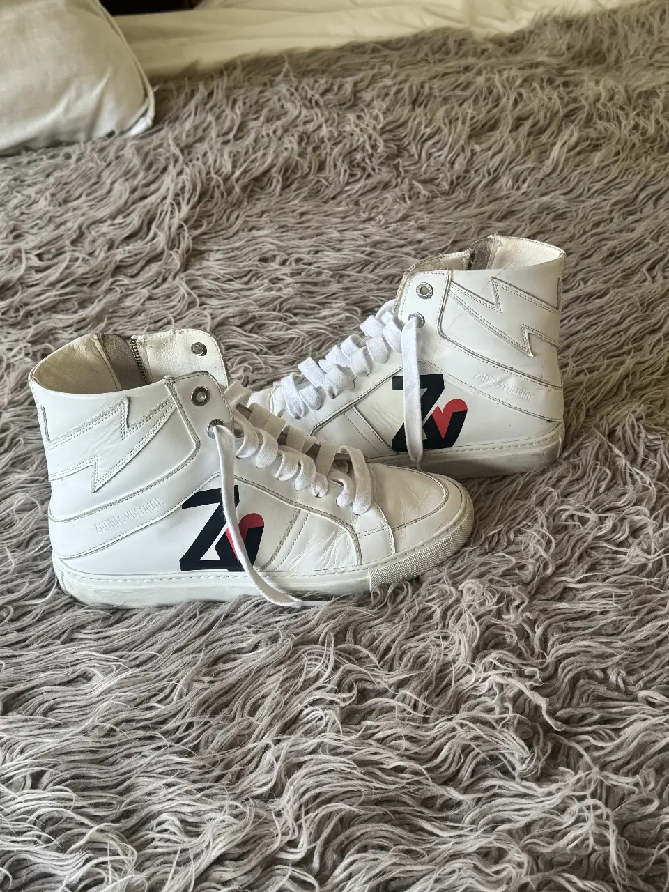 Zapatillas Zadig & Voltaire de cuero blancas con detalles en negro y rojo. Diseño de caña alta con cierre lateral y logo de la marca.