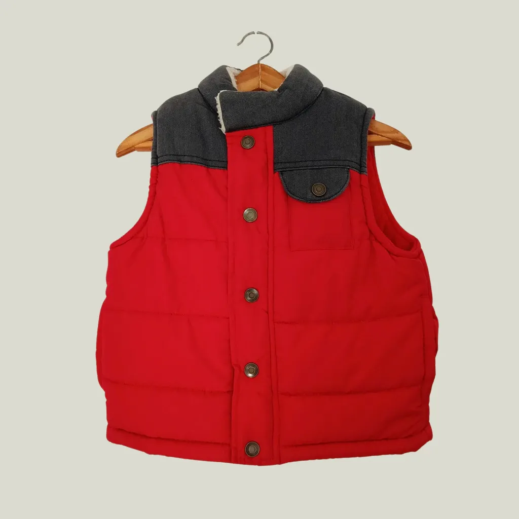 Chaleco acolchado rojo con detalles en gris oscuro en el cuello y bolsillos. Posee botones al tono y forro interior blanco.