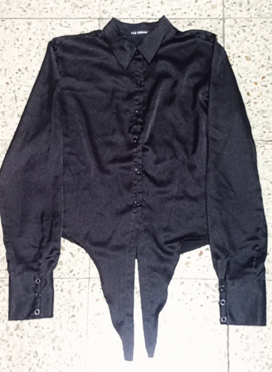 Camisa negra de seda con mangas largas y botones al frente. Posee un diseño único en la parte trasera que se cruza y se ata, dándole un toque moderno y sensual. Ideal para looks de noche o para darle un toque chic a tu outfit.