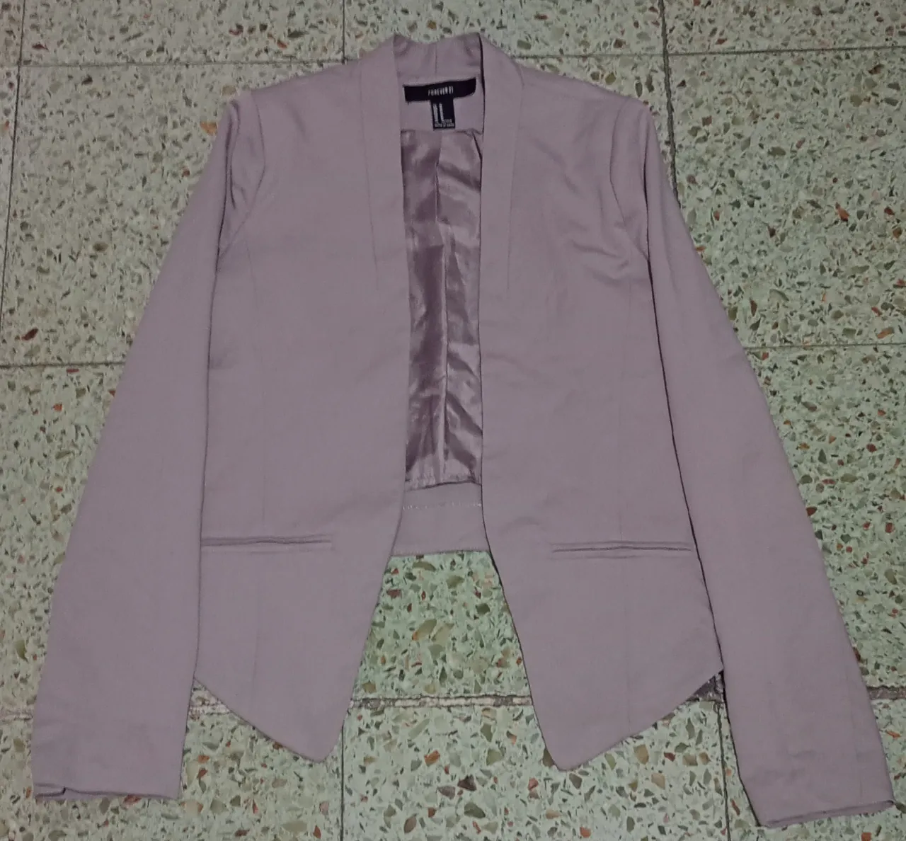 Blazer de corte moderno en color lila suave. Diseño abierto sin botones, con solapas finas y bolsillos falsos en la parte delantera. Ideal para un look elegante y sofisticado.