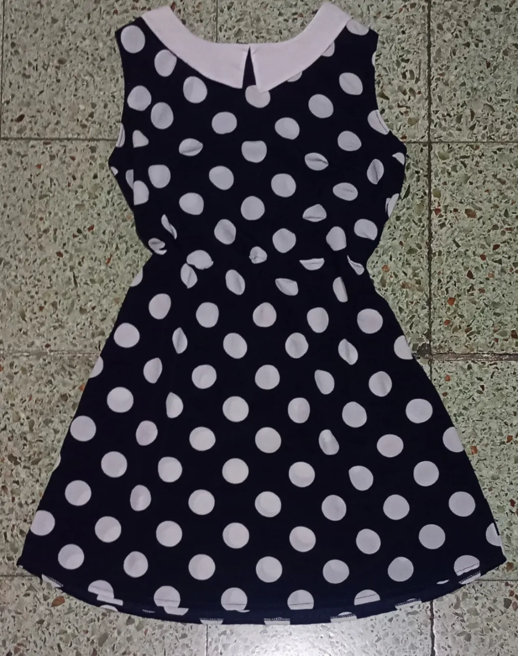 Vestido negro con lunares blancos, cuello blanco y sin mangas. Ideal para un look retro y divertido.